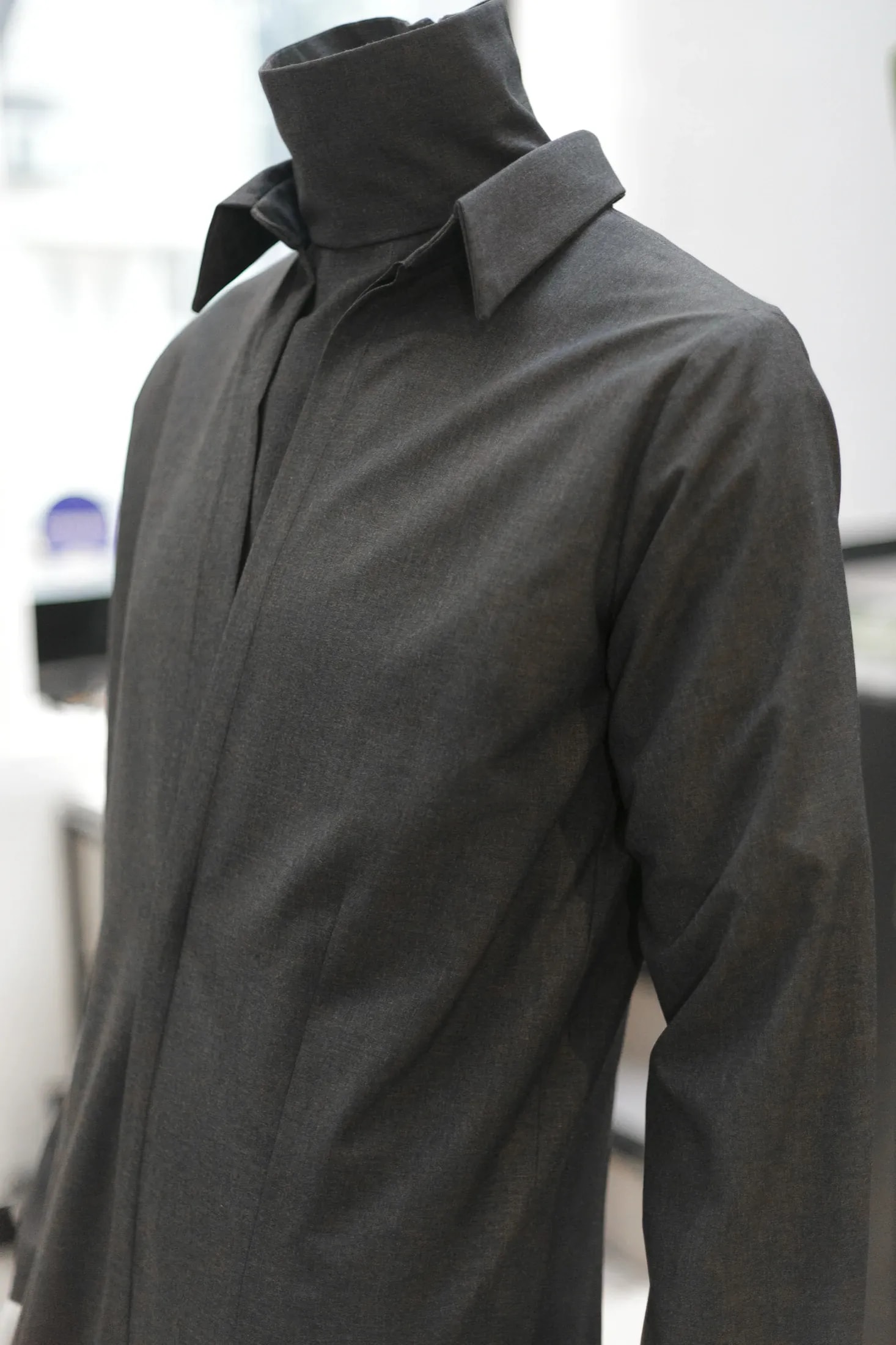 Detalle del cuello camisero alto y el cierre frontal oculto del jumpsuit sastrero gris, vista de tres cuartos sobre maniquí.