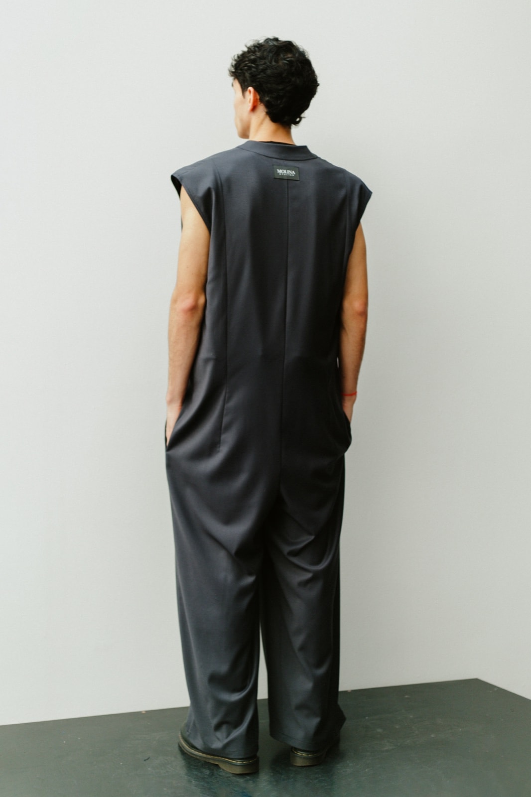 Espalda del jumpsuit sastrero gris sin mangas, con costura central y hombros estructurados.