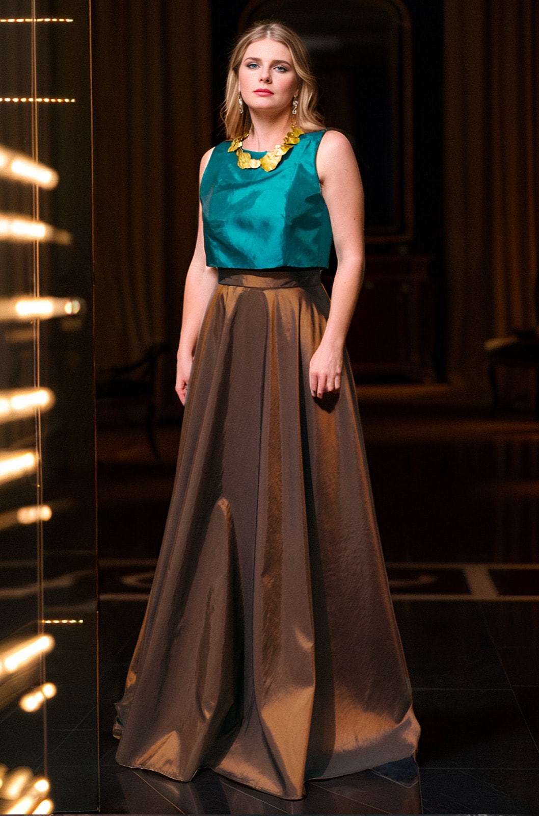 Maxi-falda de tafetán de seda color chocolate de Atelier Molina, combinada con top verde esmeralda sin mangas, en un salón con luces cálidas.