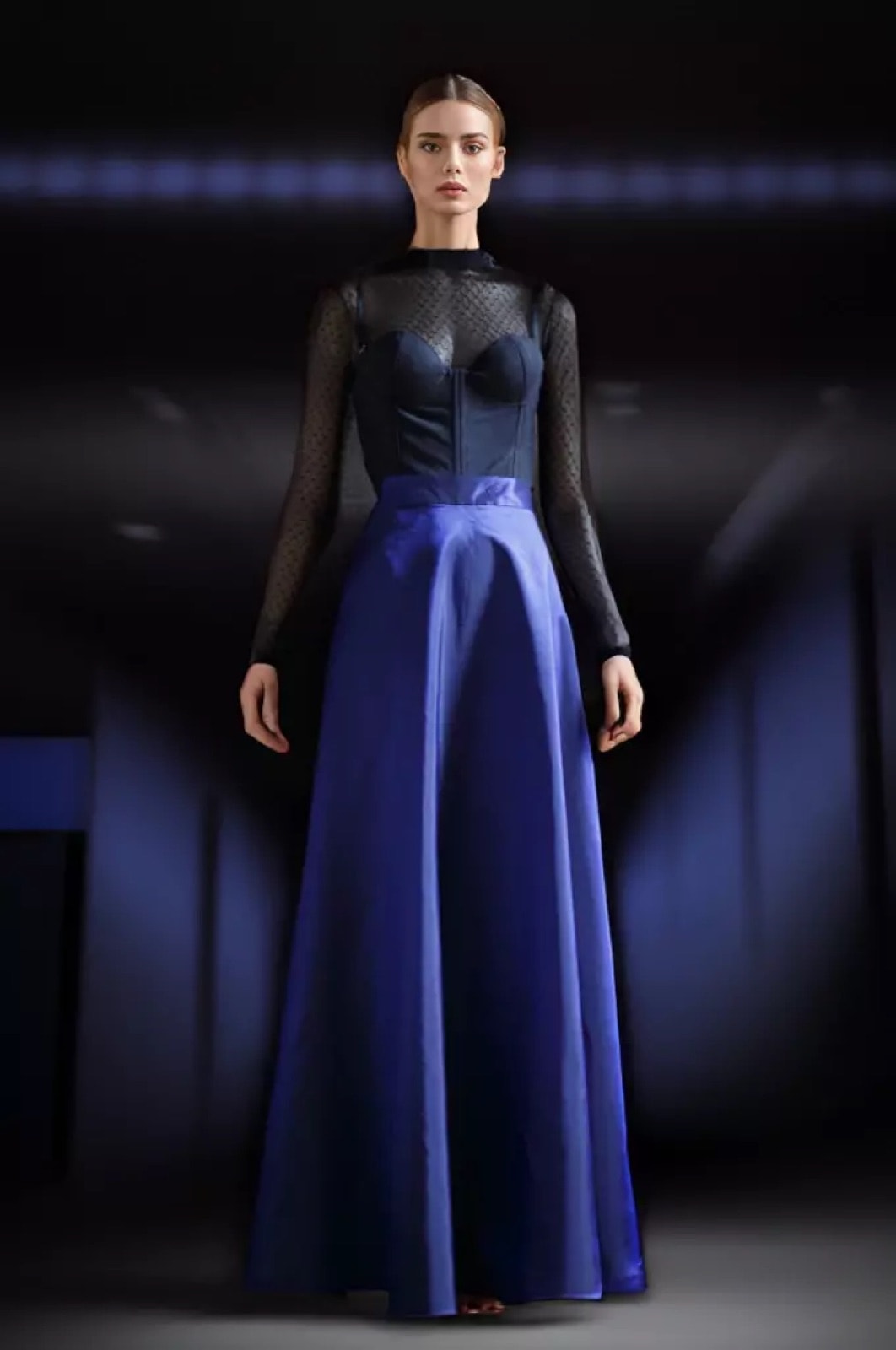 Maxi-falda de tafetán de seda azul índigo de Atelier Molina, sobre modelo con top negro transparente y corsetería, fondo oscuro iluminado en azul.