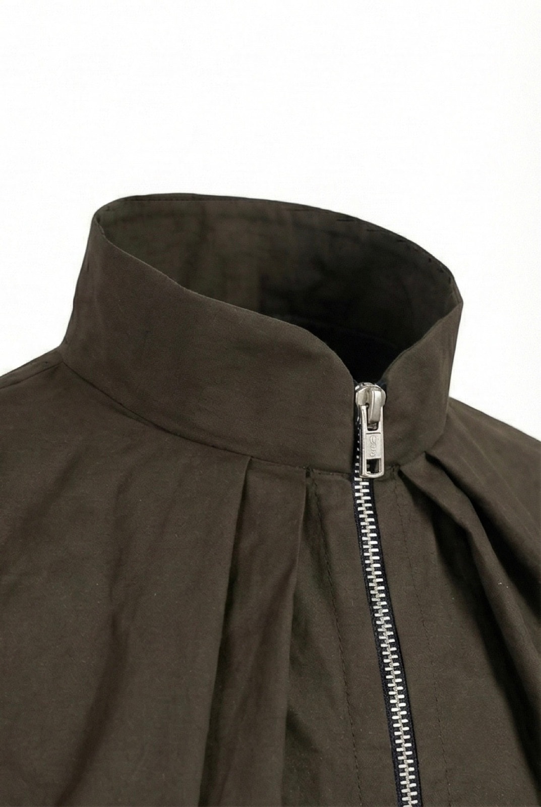 Detalle del cuello alto y el cierre metálico de la campera impermeable verde oliva, con las tablas del pliegue delantero.