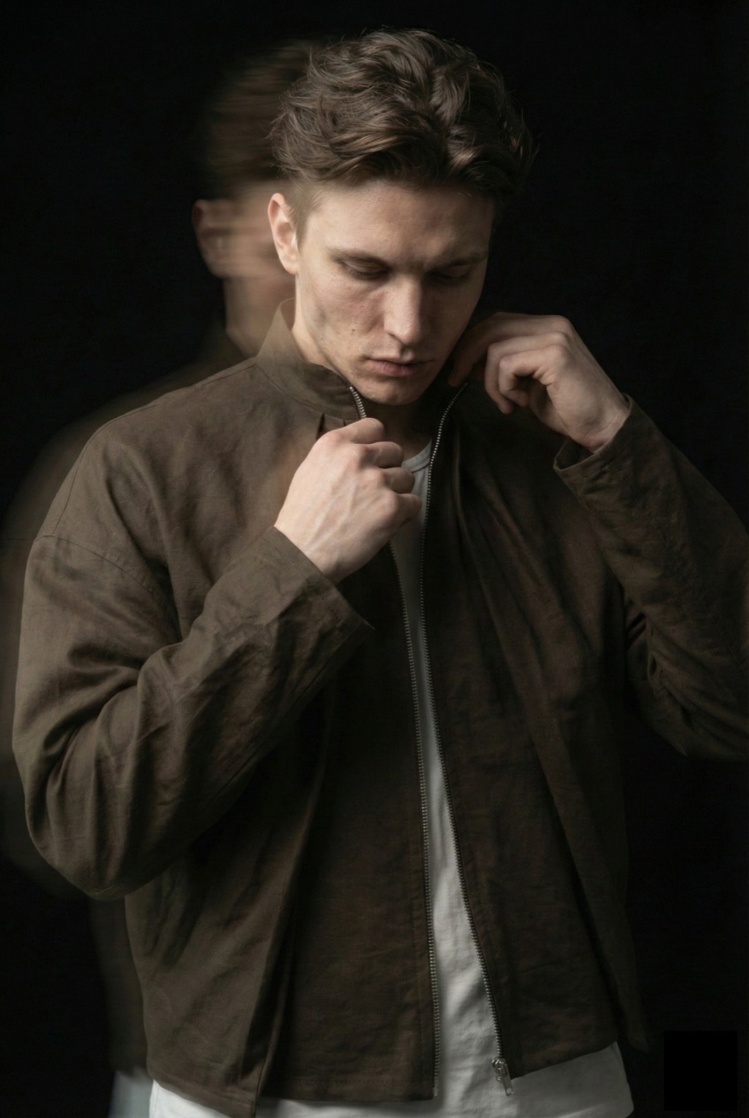 Campera impermeable verde oliva sobre modelo cerrando el cierre hasta el cuello, con las manos en el mentón.