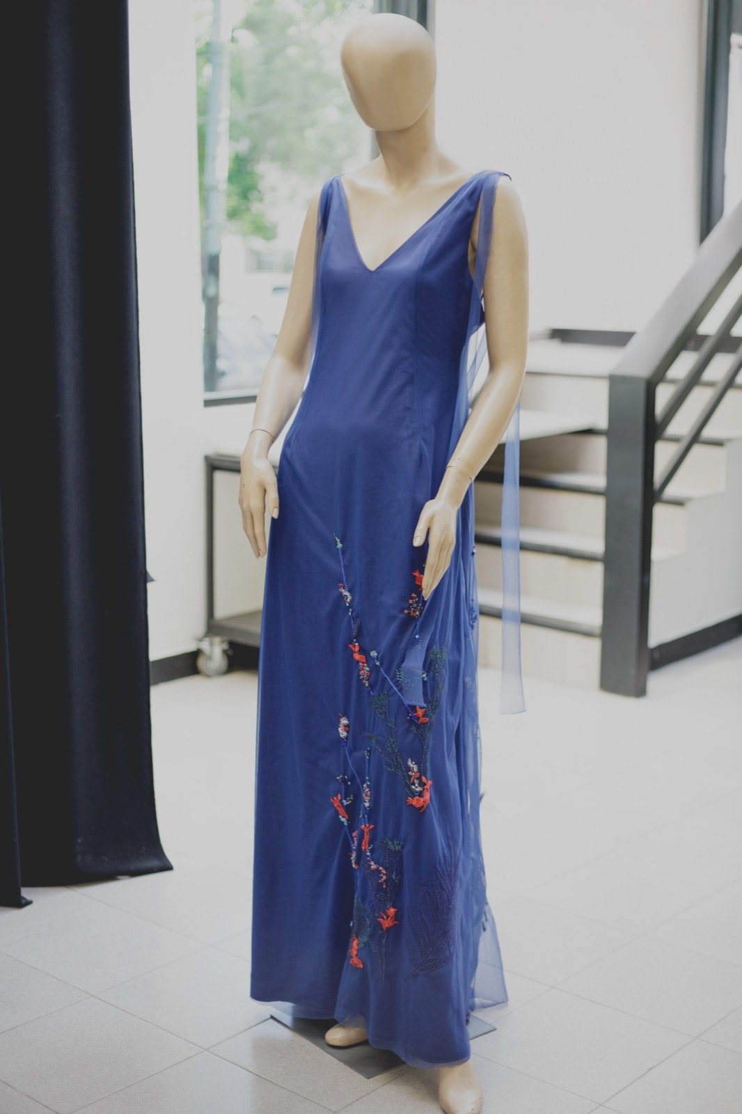 Nigh Blue Garden Dress sobre maniquí junto a una ventana, con el tul azul cayendo desde el hombro.