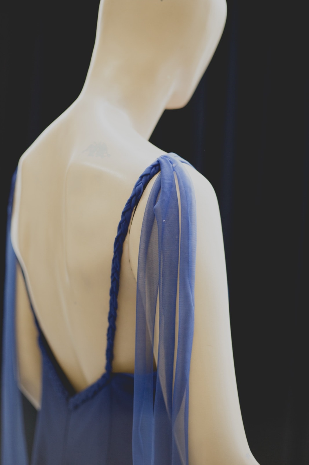 Detalle de la espalda descubierta y la tira trenzada del Nigh Blue Garden Dress sobre maniquí, con tul suelto en el hombro.