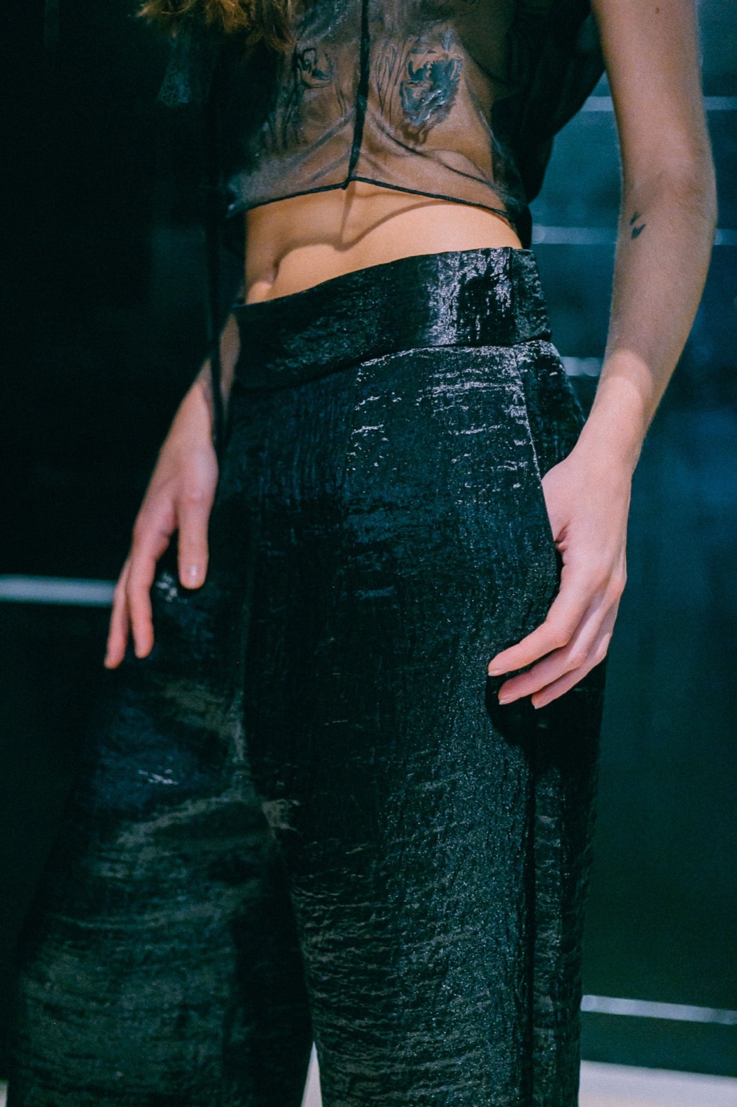 Detalle de la cintura del pantalón ancho texturado negro con la mano en el bolsillo, sobre modelo en backstage.