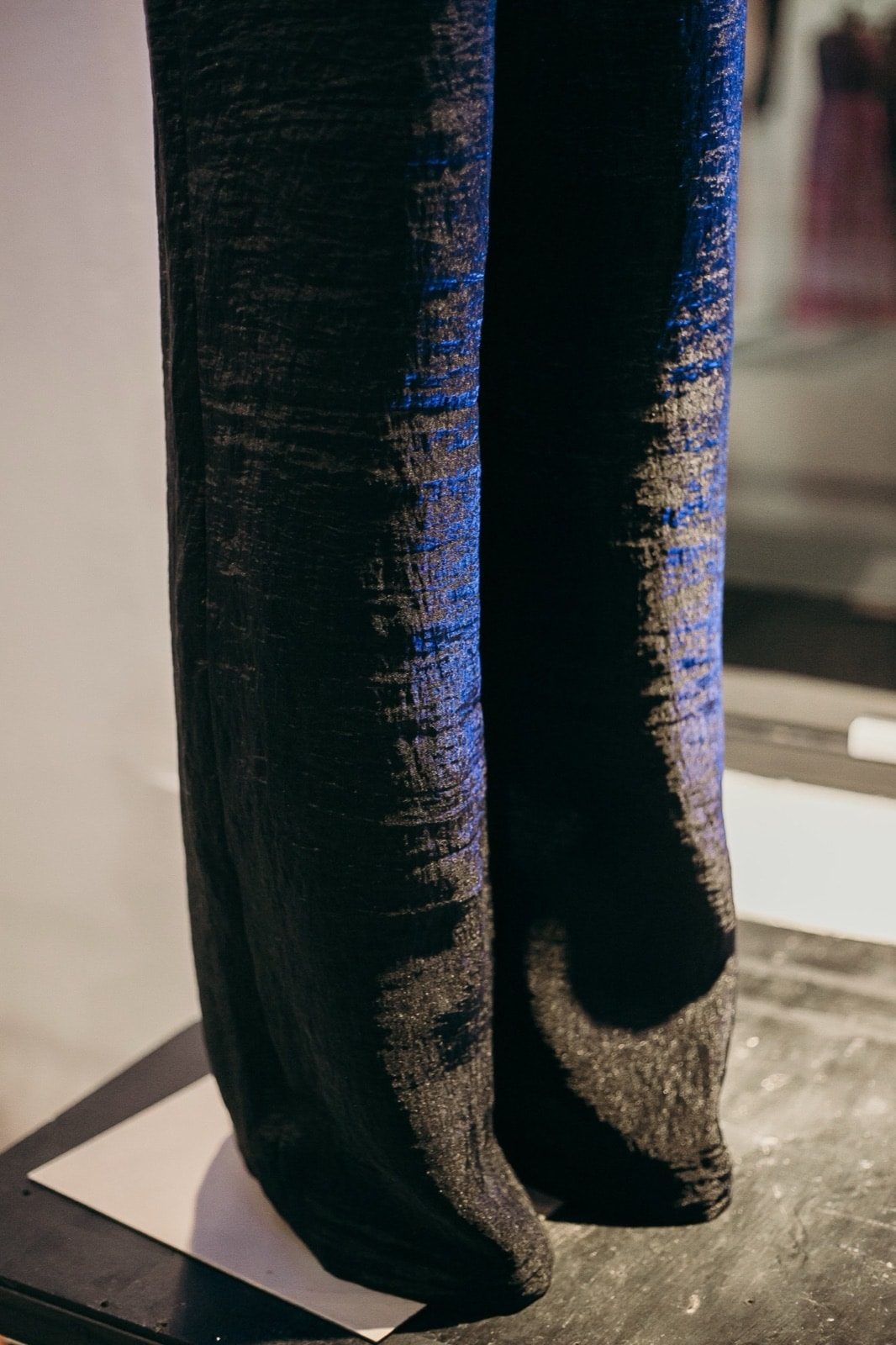 Detalle del ruedo ancho del pantalón texturado negro apoyado sobre la base de exhibición del atelier.