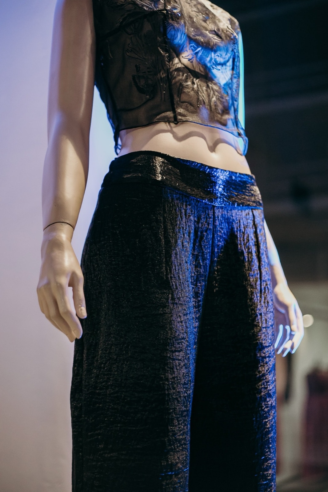 Detalle de la cintura del pantalón ancho texturado negro sobre maniquí, con las manos apoyadas a los costados.