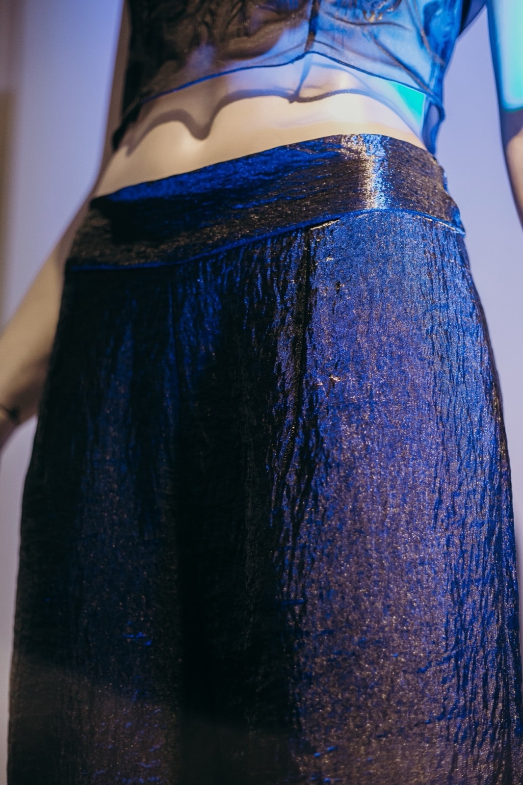 Detalle de la cintura del pantalón ancho texturado negro, vista de espalda sobre maniquí con reflejos azulados.