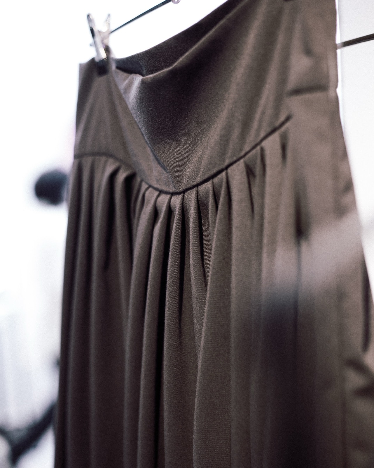 Detalle de las tablas en la cintura del pantalón chiripá gris oscuro, en primer plano sobre percha.