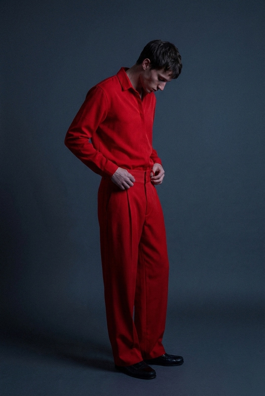 Pantalón sastrero rojo de crepe de Atelier Molina, vista de perfil sobre modelo con camisa a tono, fondo gris oscuro.