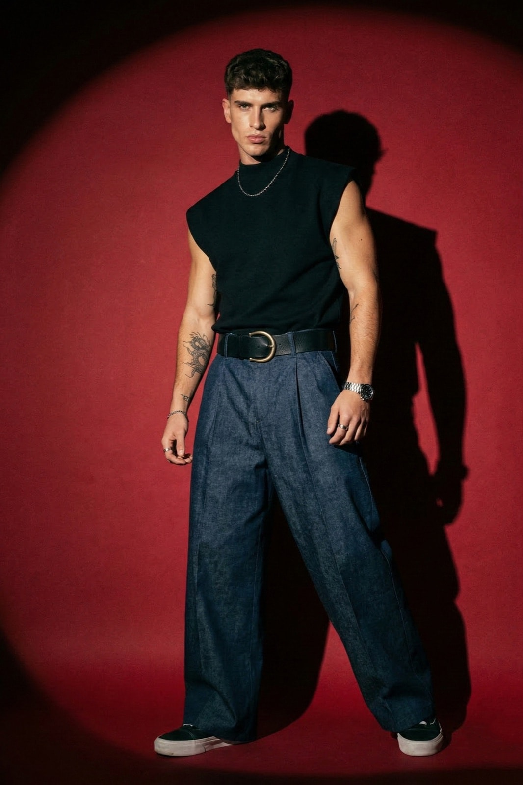 Pantalón Sastrero Molina en denim raw índigo sobre modelo con musculosa negra y cinturón, vista frontal sobre fondo rojo.