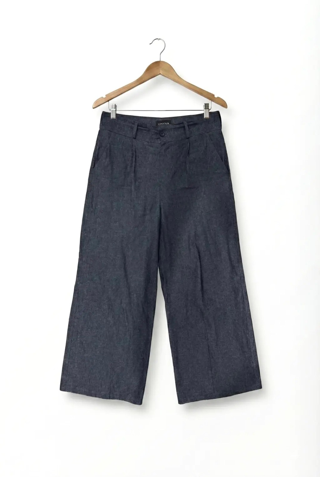 Pantalón Sastrero Molina en denim raw índigo colgado en percha, vista frontal de producto con pinzas y bolsillos delanteros.