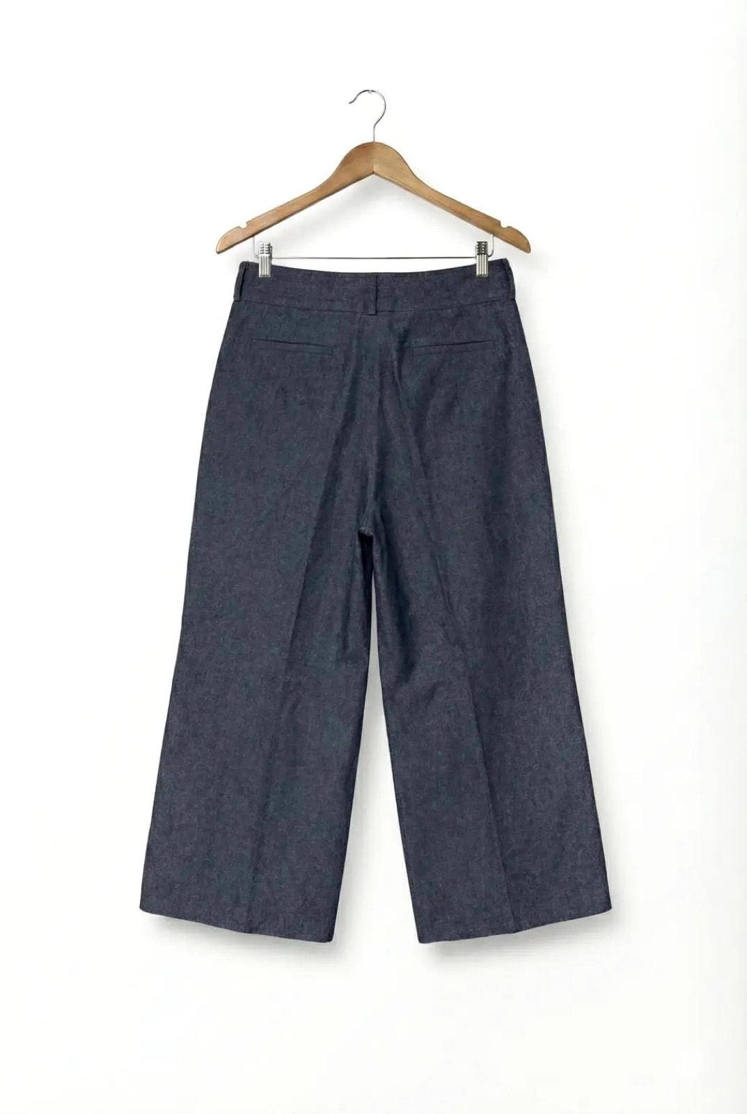 Pantalón Sastrero Molina en denim raw índigo colgado en percha, vista de espalda con los bolsillos traseros.