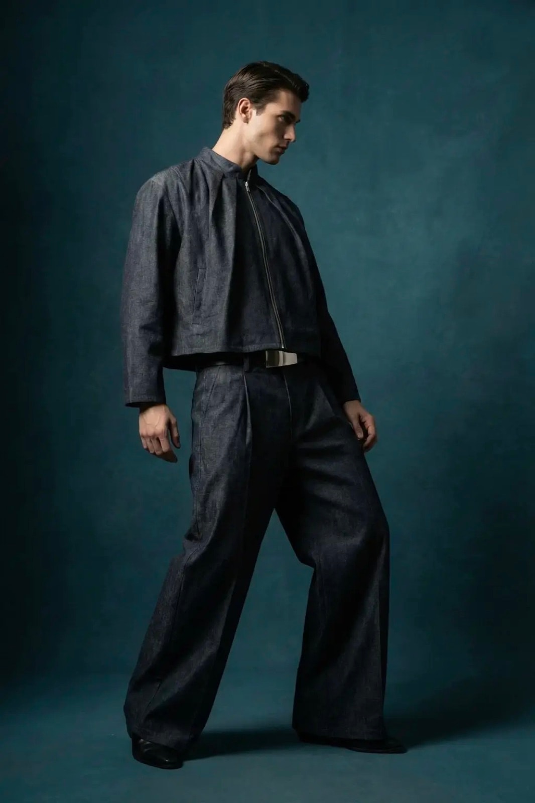 Pantalón Sastrero Molina en denim raw índigo sobre modelo caminando, combinado con campera a juego sobre fondo azulado.