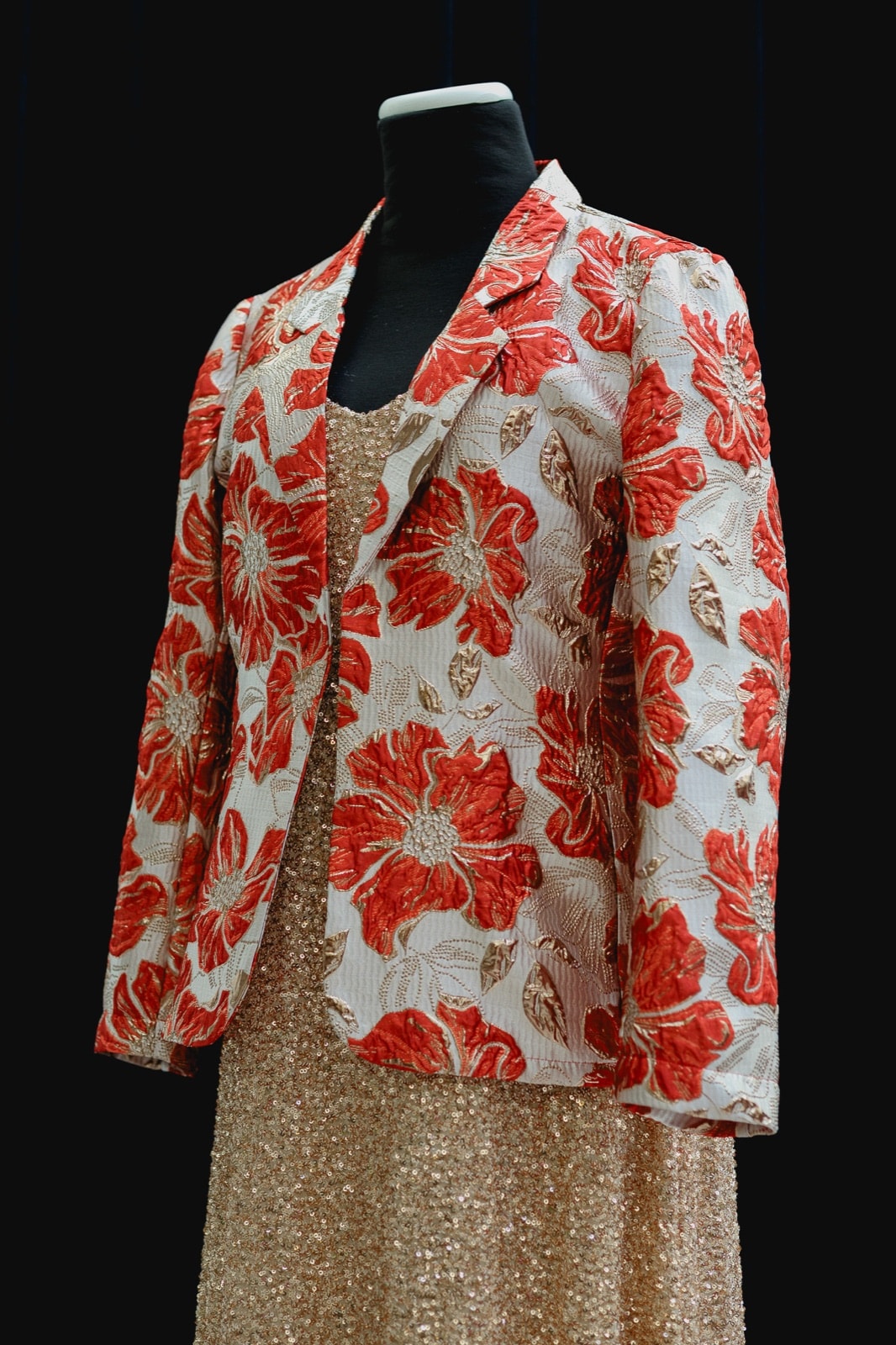 Saco de brocato con estampa floral roja y dorada de Atelier Molina sobre maniquí, vista de tres cuartos con falda de lentejuelas doradas.