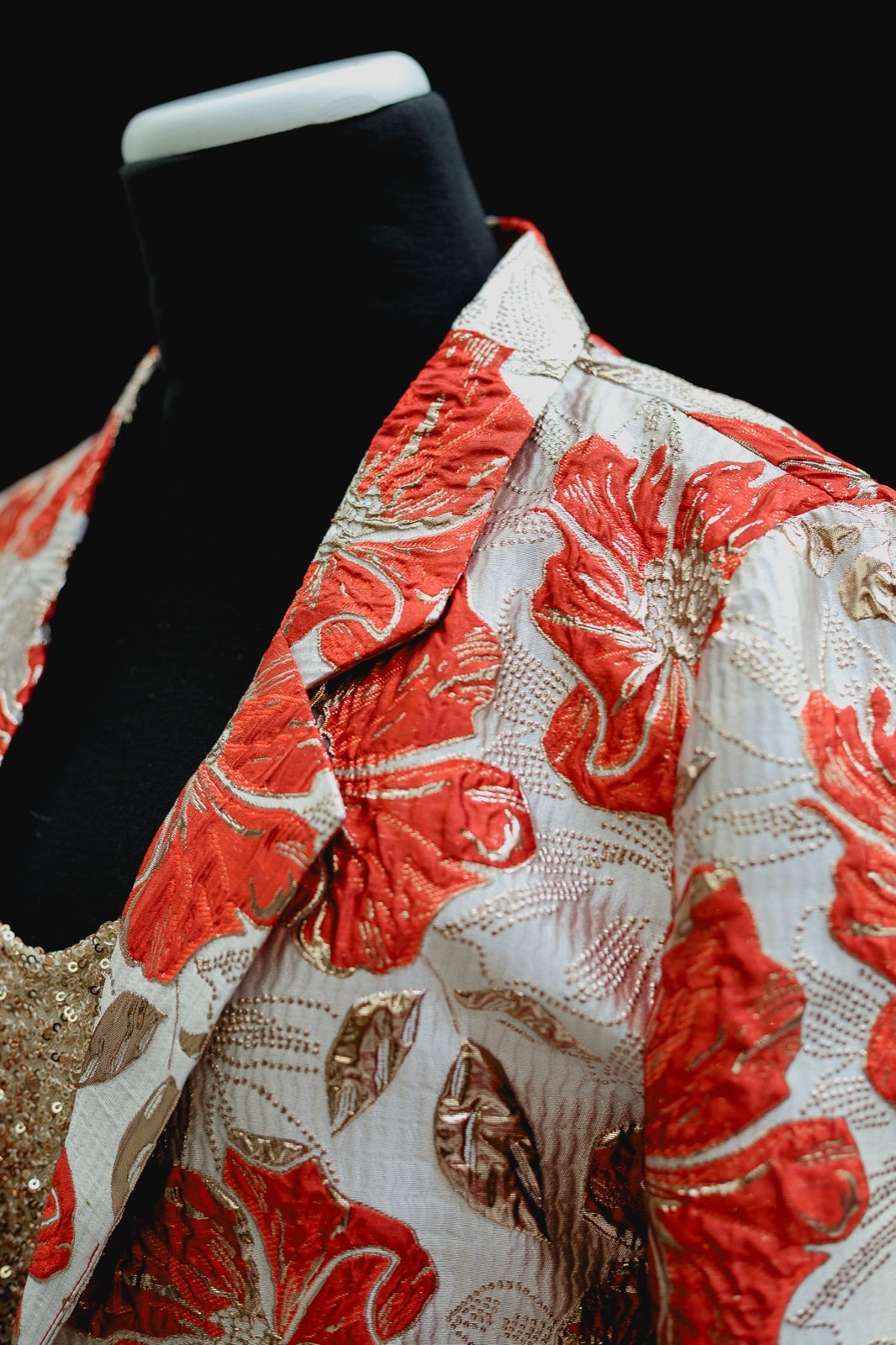 Detalle de la solapa y el bordado floral rojo y dorado del saco de brocato de Atelier Molina, primer plano sobre maniquí.