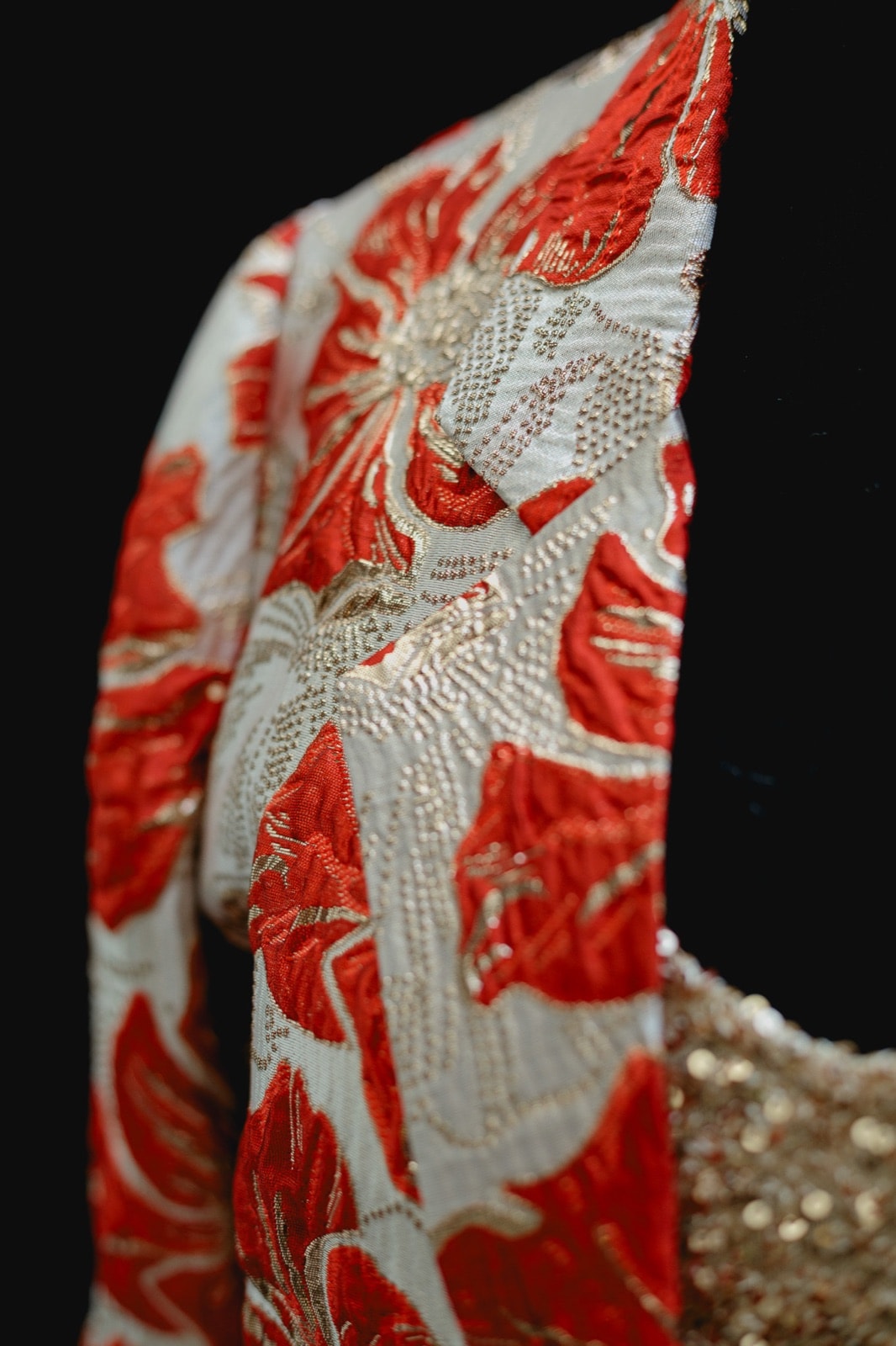 Detalle de la manga del saco de brocato con flores rojas y doradas de Atelier Molina, primer plano de la textura del tejido.