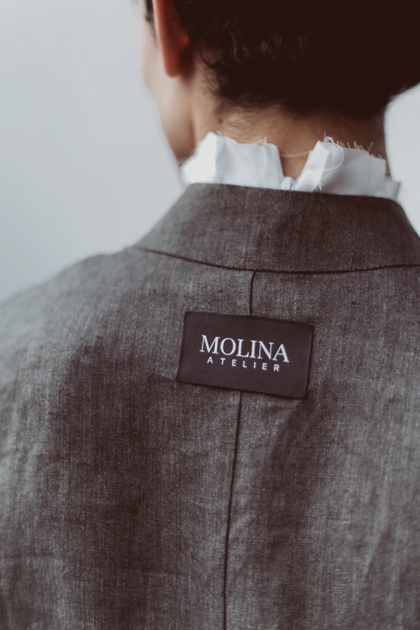 Espalda de la Chaqueta Molina de lino italiano verde alga de Atelier Molina, con la etiqueta Molina Atelier cosida al centro, sobre una camisa blanca de cuello alto con los bordes al descubierto. Diseñada y confeccionada en nuestro atelier de Buenos Aires.