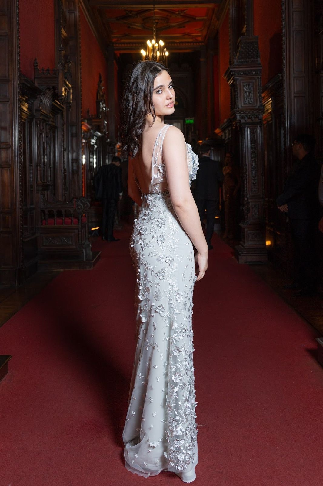 Espalda descubierta del vestido de tul plateado bordado de Atelier Molina, sobre modelo en un pasillo con candelabros y alfombra roja.