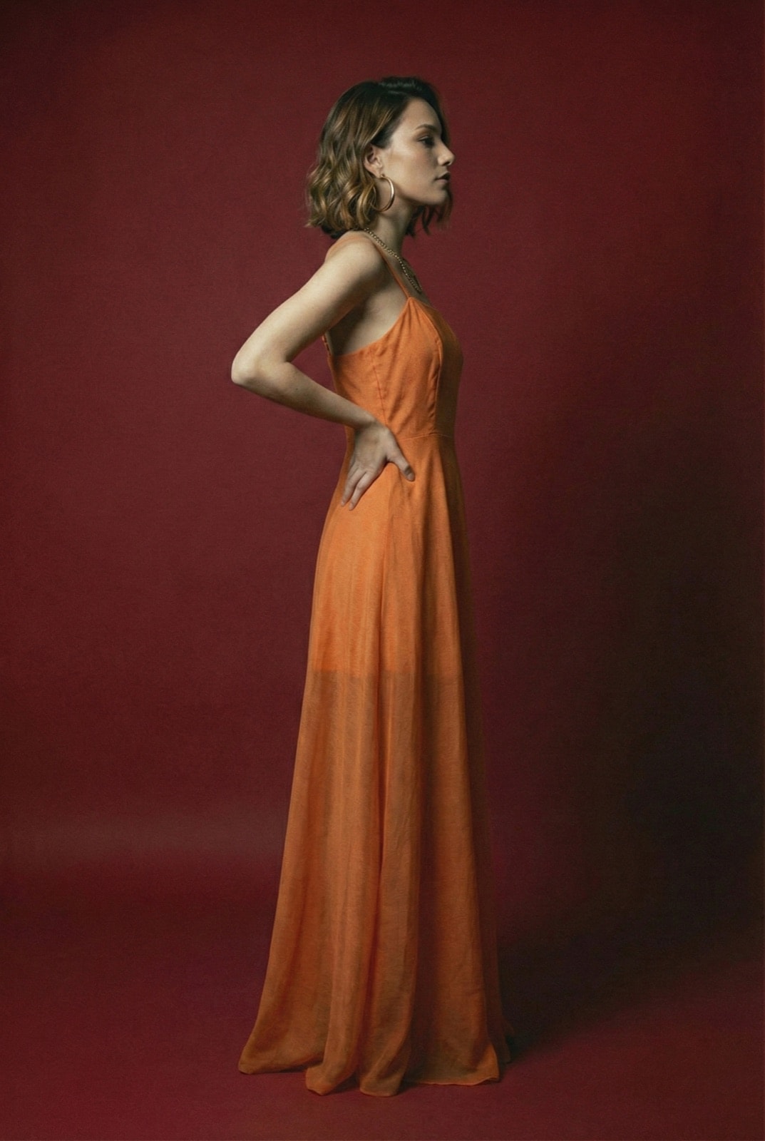 Sunset Glow Dress naranja sobre modelo, vista de perfil que muestra la caída fluida de la falda hasta el piso.