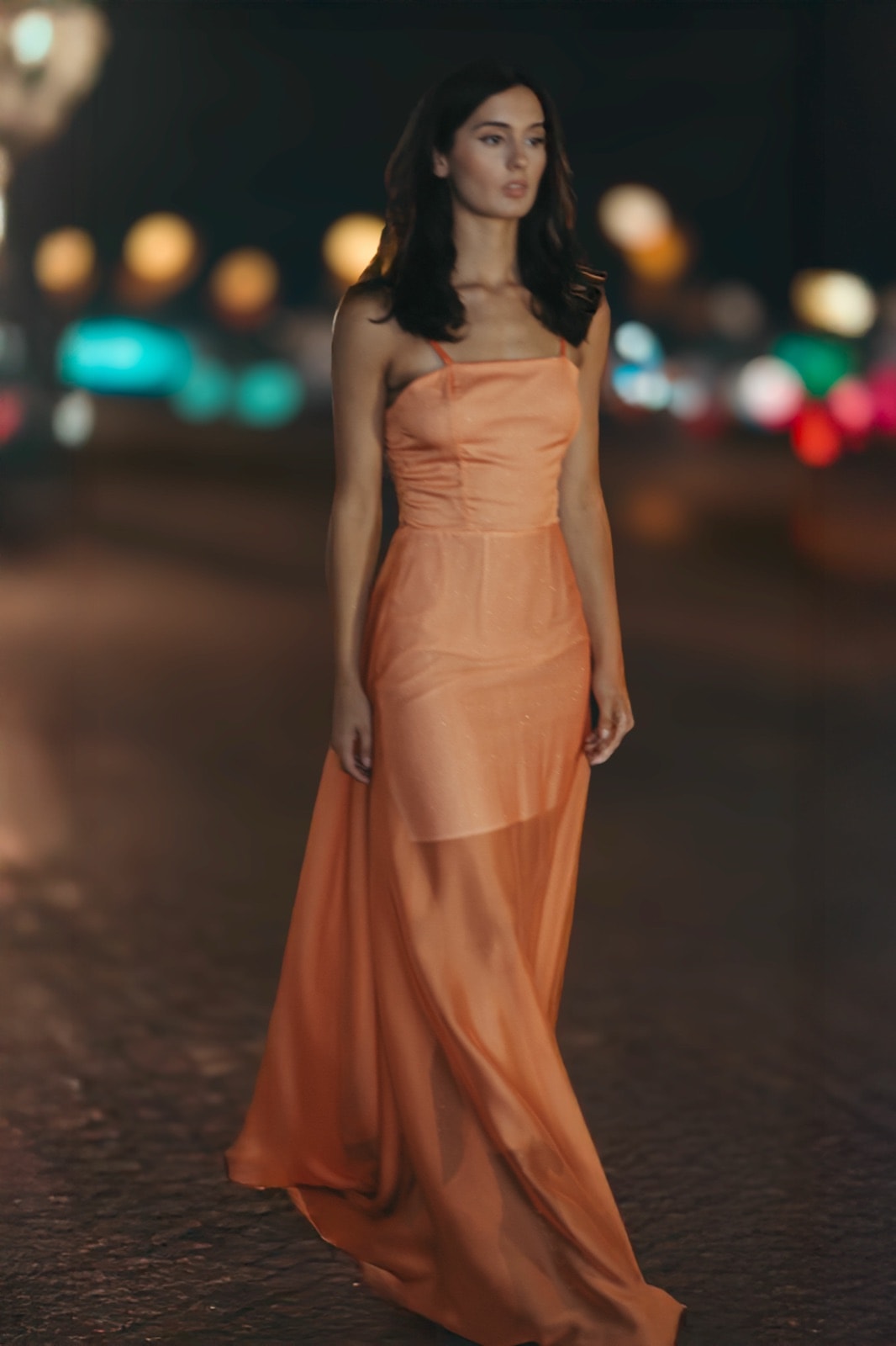 Sunset Glow Dress naranja sobre modelo caminando de noche por una calle iluminada, con la falda semitransparente en movimiento.