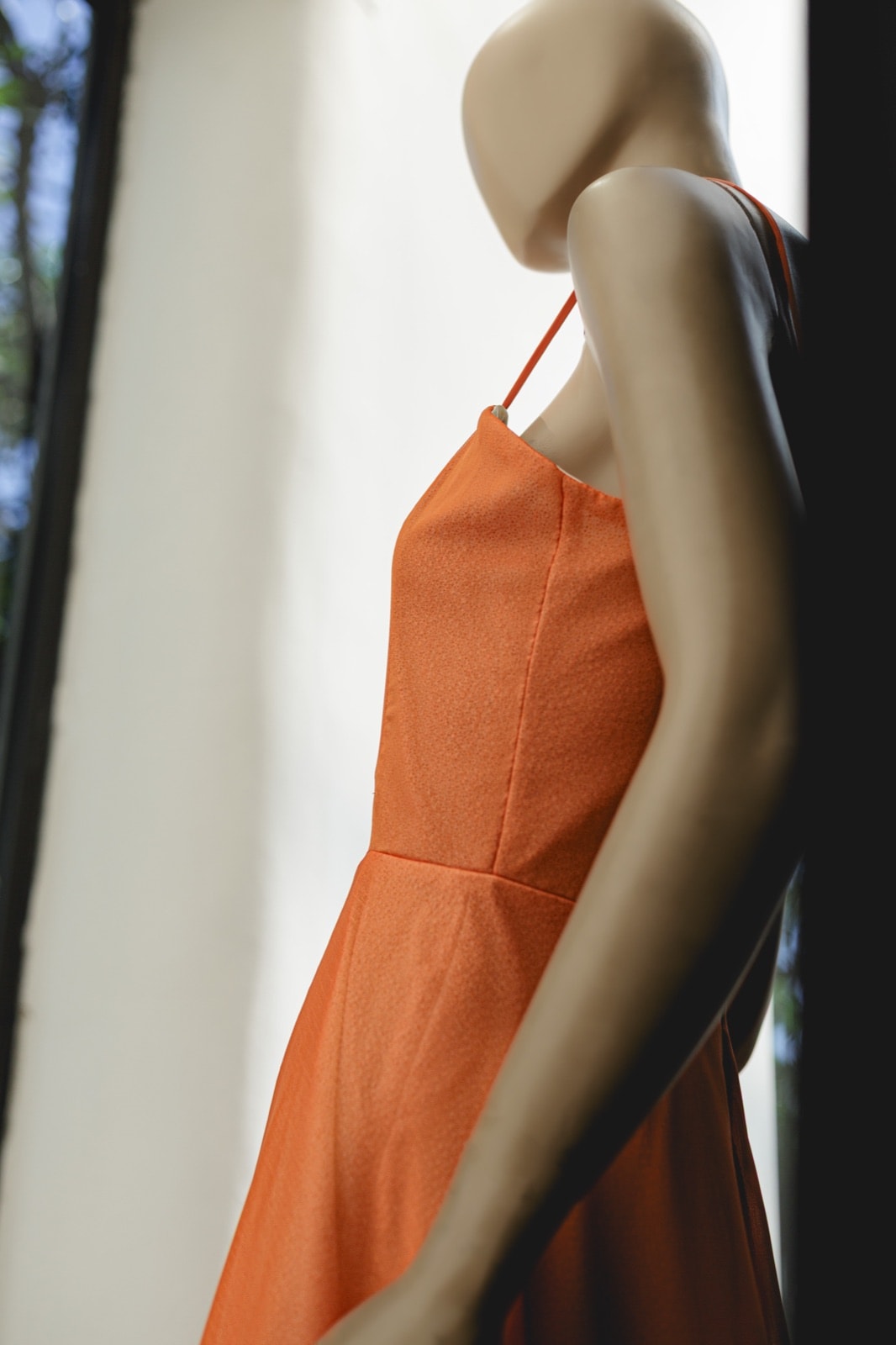 Detalle del tirante y el escote del Sunset Glow Dress naranja sobre maniquí, primer plano en vidriera.