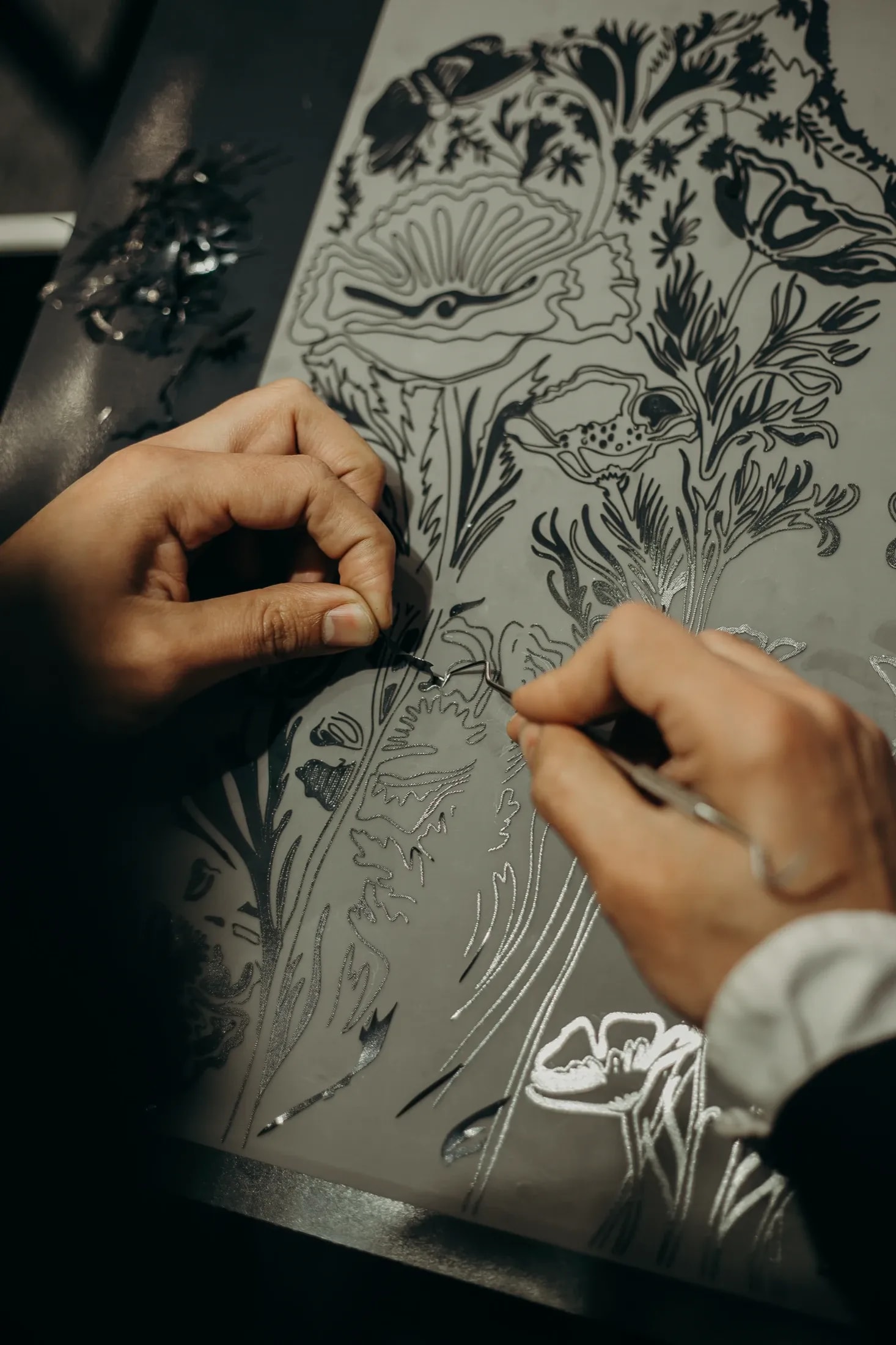 Primer plano de las manos retirando con una herramienta el vinilo sobrante de un diseño floral, durante la confección.