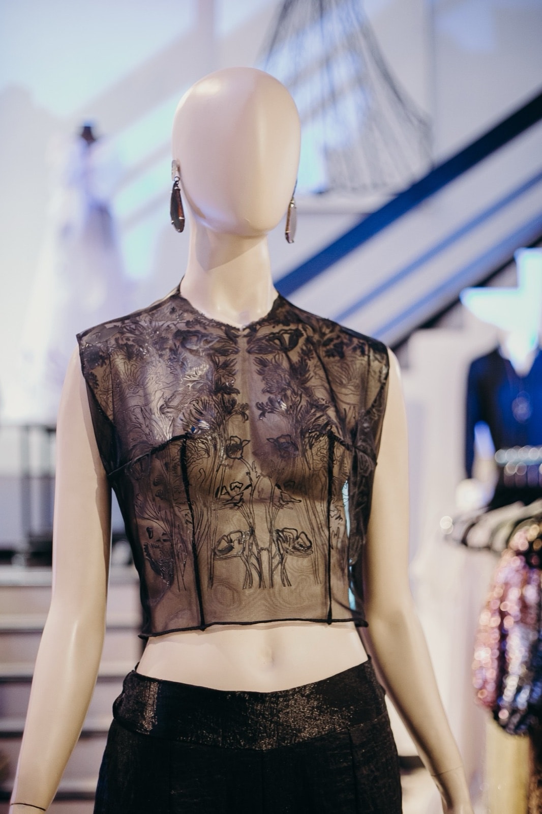 Top Tattoo en tul negro transparente sobre maniquí, con el estampado de figuras y flores a la altura del pecho en el showroom.