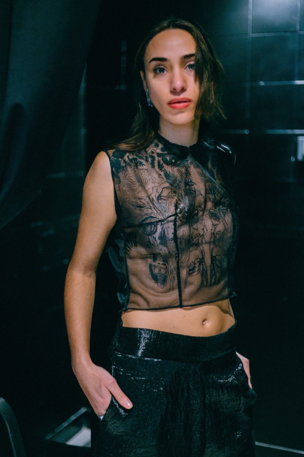 Top Tattoo en tul negro transparente, primer plano frontal que muestra el estampado ilustrado sobre fondo oscuro reflectante.