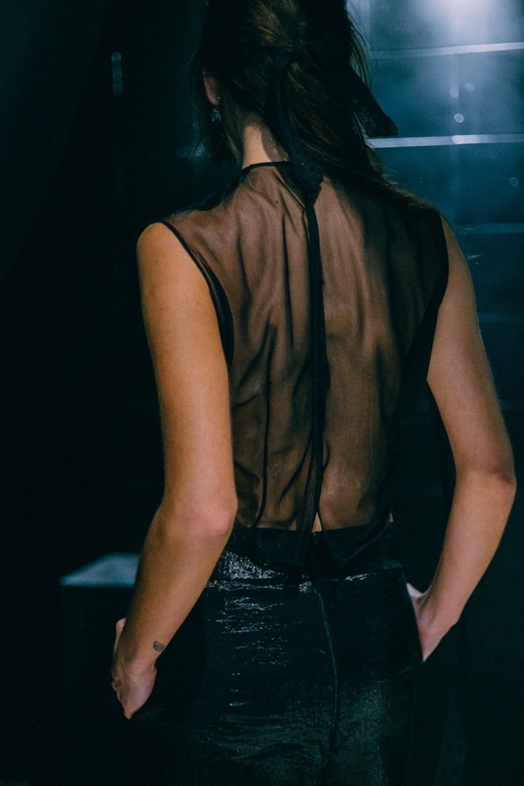 Vista trasera del Top Tattoo en tul negro transparente, con la espalda descubierta y el cierre de tira sobre fondo oscuro.