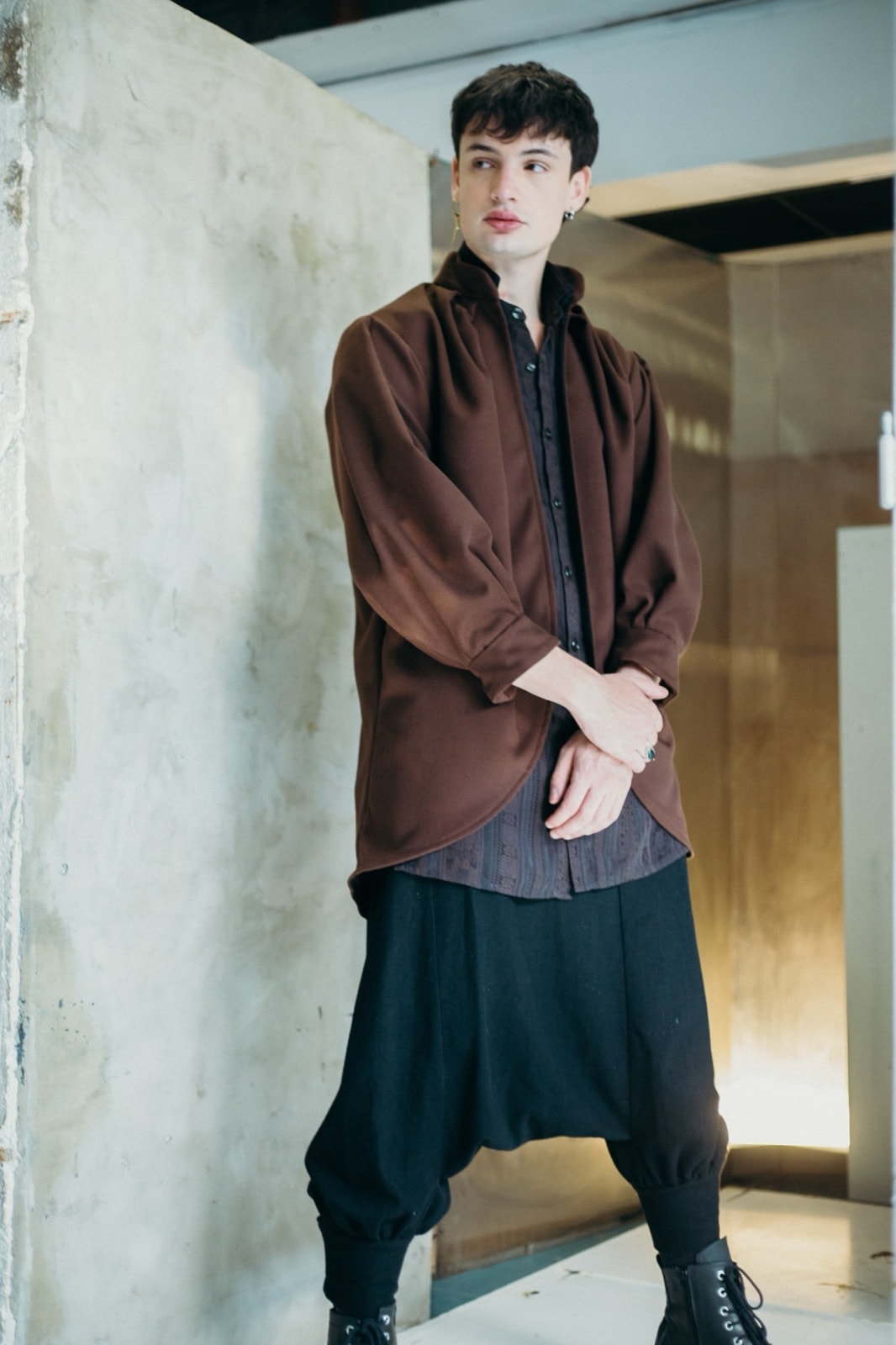 Saco tulip chocolate de Atelier Molina sobre modelo de cuerpo entero, apoyado en un vano de cemento junto a pantalón negro amplio.
