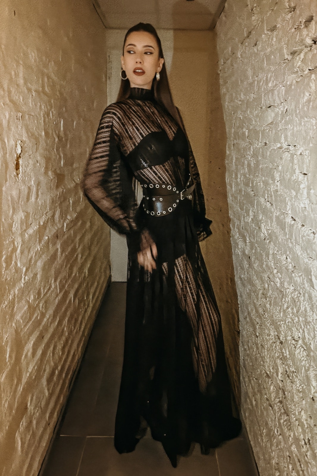Vestido de encaje vertical elastizado negro sobre modelo, vista frontal completa en un pasillo de paredes de piedra clara.