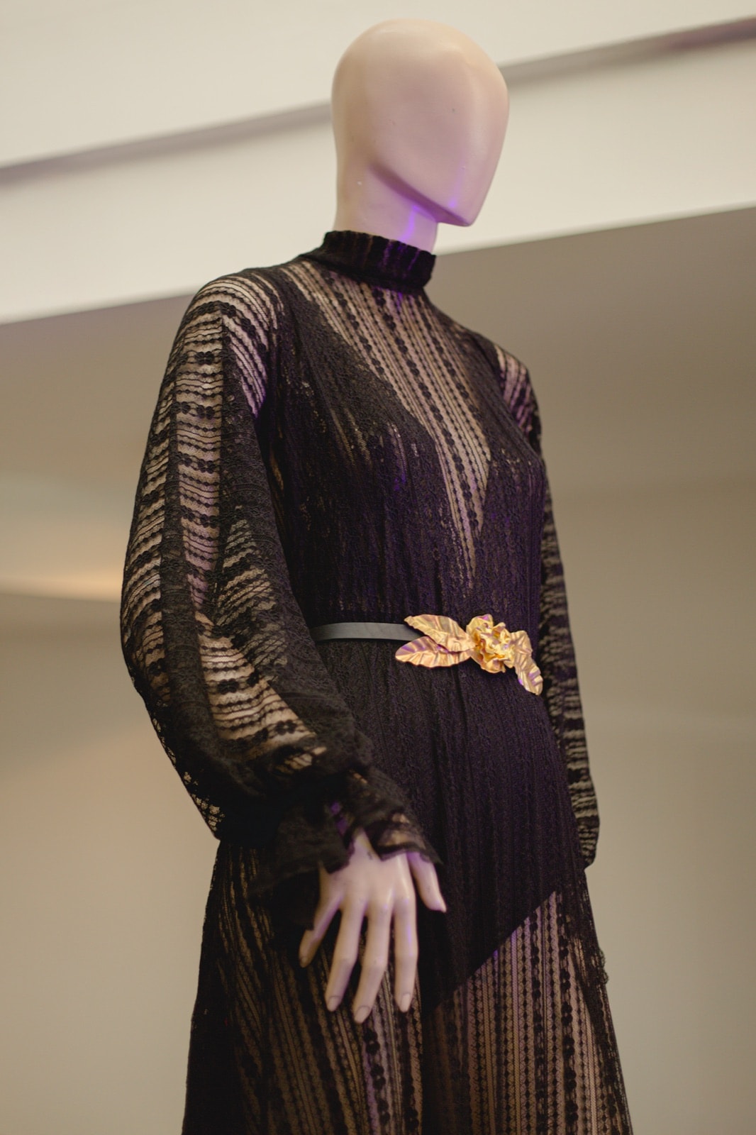 Detalle del cuello alto y el cinturón floral del Vestido de encaje vertical elastizado negro, sobre maniquí en vidriera.