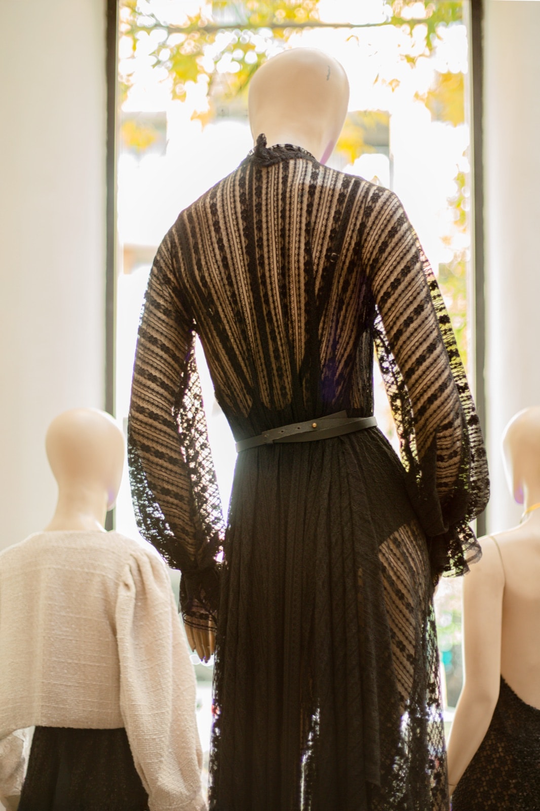 Vestido de encaje vertical elastizado negro sobre maniquí, vista de espalda junto a una ventana con luz natural.