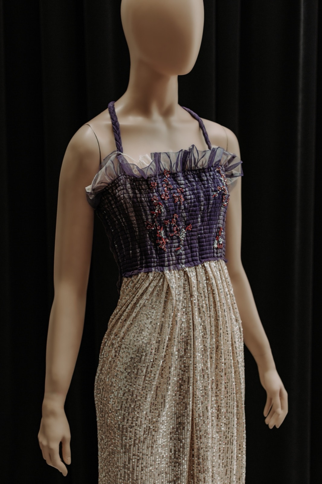 Vestido drapeado violeta bordado sobre maniquí, vista frontal con el bustier fruncido y la falda de paillete dorado.