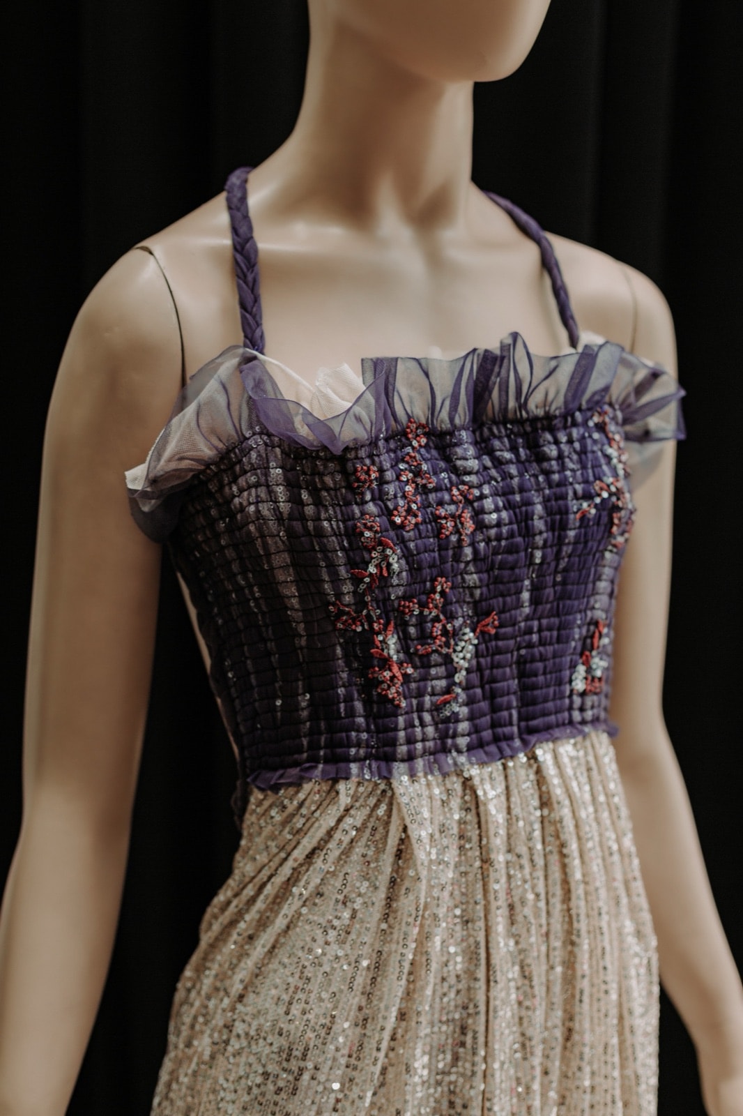 Detalle del bustier drapeado violeta con bordado floral en cuentas, primer plano sobre maniquí con tul en el borde.