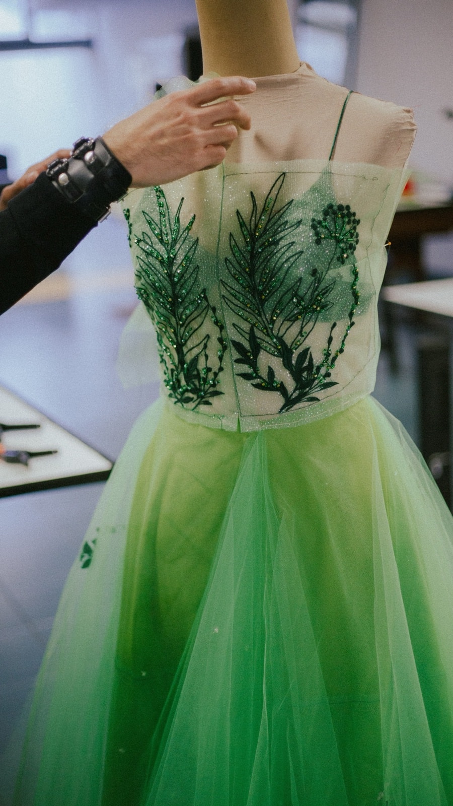 Corpiño bordado del vestido Emerald Garden en proceso de armado sobre maniquí de sastrería, con una mano ajustando el bretel.