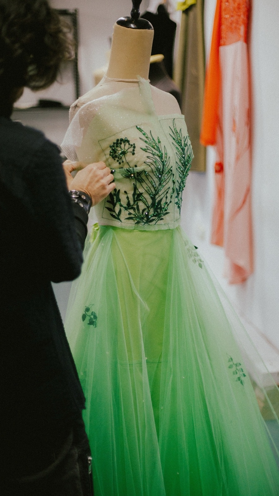 Corpiño bordado del vestido Emerald Garden sobre maniquí de atelier, con una mano ajustando la costura durante la confección artesanal.