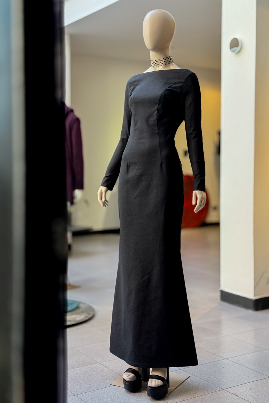 Vestido largo negro de gabardina de Atelier Molina sobre maniquí, vista de tres cuartos en el interior del showroom.
