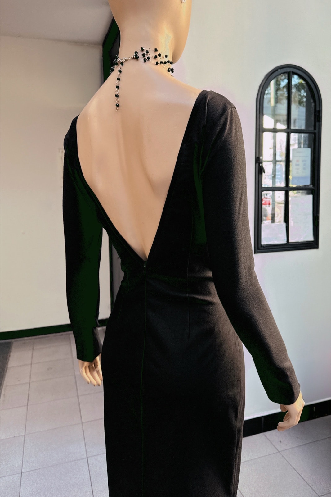 Detalle de la espalda descubierta y el cierre invisible del vestido largo negro de gabardina de Atelier Molina, sobre maniquí.