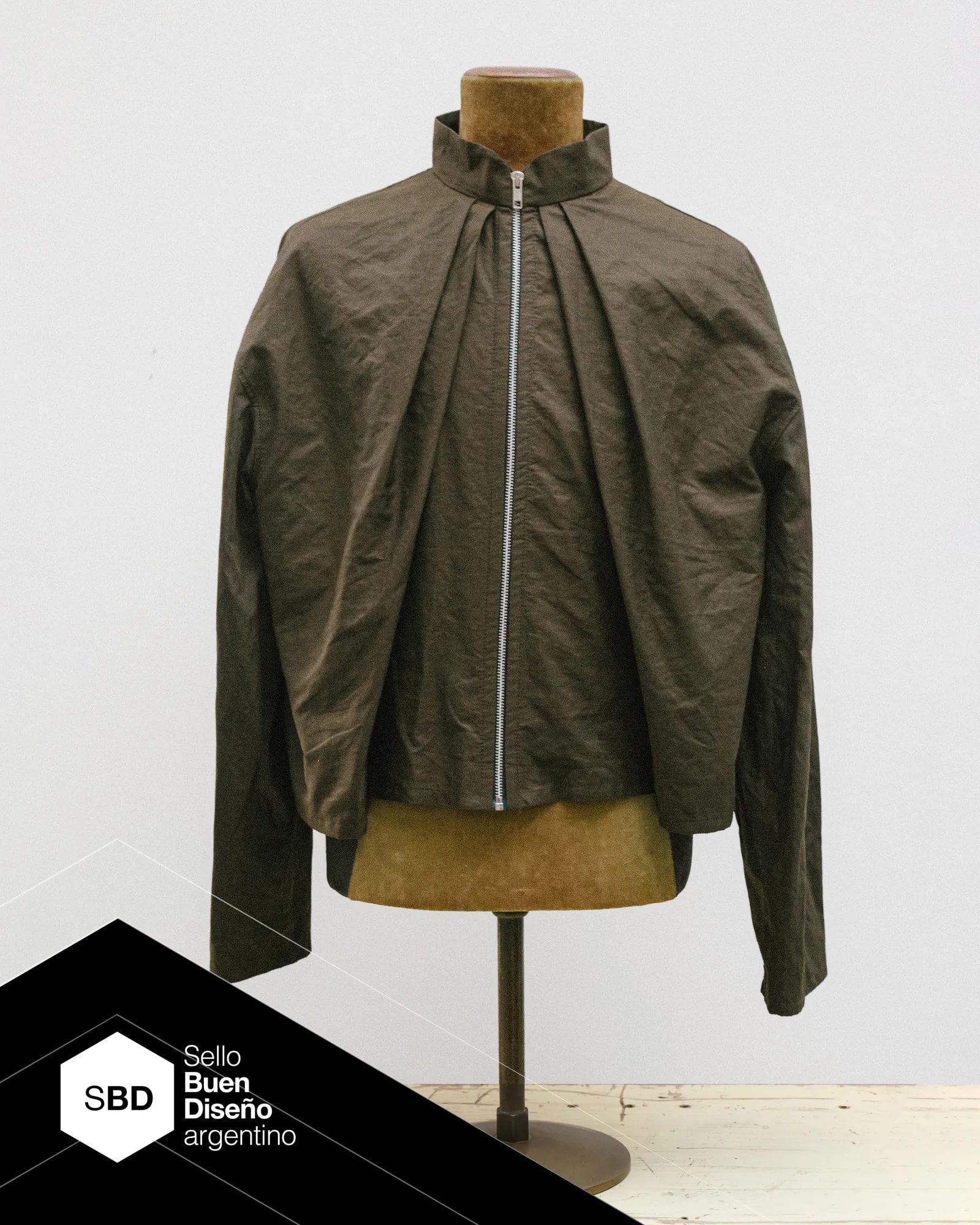 Water repellent Molina Jacket in olive recycled PET fabric, with two front pleats set at 45 degrees. Part of the Atelier Molina PLIEGO line, Argentine Good Design Seal 2026, made in Buenos Aires.