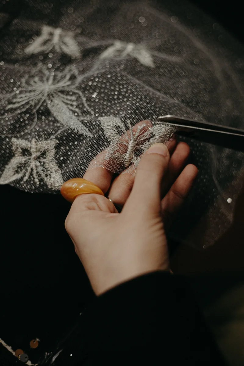 Manos separando un encaje bordado con tijera, durante las prácticas profesionales de la FADU (UBA) en Atelier Molina