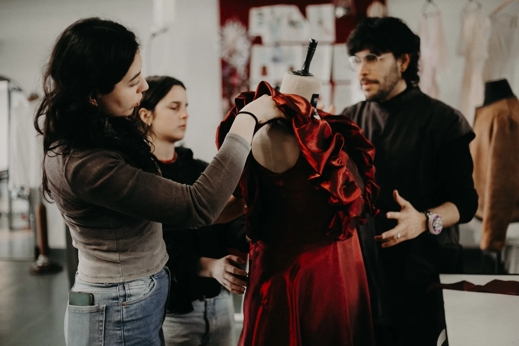 Dos estudiantes de la FADU (UBA) y Carlos Molina trabajando un vestido rojo sobre el maniquí en el atelier de Buenos Aires