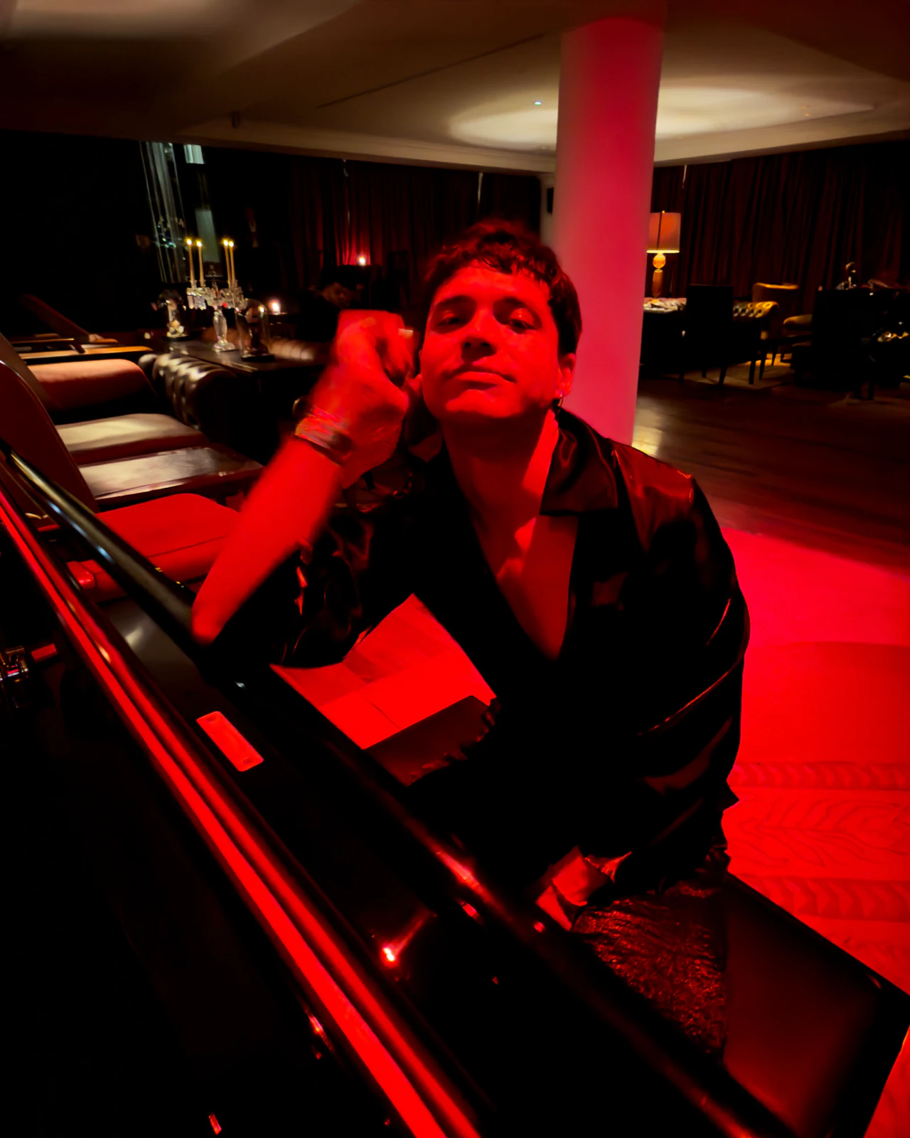 Alan Lez leaning on a grand piano in a black satin shirt by Atelier Molina